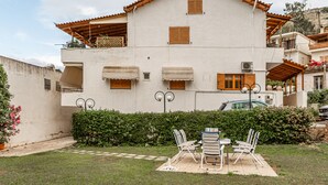 Un edificio de dos pisos con techo de tejas, balcones y un jardín con mobiliario exterior.