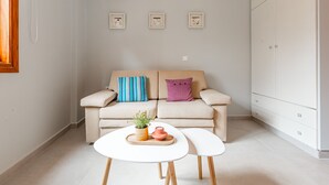 Una sala moderna con un sofá beige, dos mesas blancas y un armario de madera.