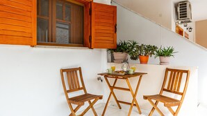 Un pequeño balcón con sillas de madera, una mesa y plantas en macetas.