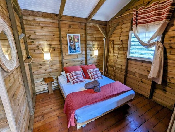 Un dormitorio de cabaña de madera con cama, almohadas, una colcha, un reloj de pared, un cartel y una ventana con cortinas.
