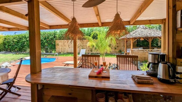 An outdoor wooden deck with a bar area, a pool, and a thatched-roof structure. - Kabane D'o, Gîte Tropical de Charme (Saint-François)