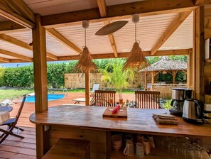 An outdoor wooden deck with a bar area, a pool, and a thatched-roof structure. - Kabane D'o, Gîte Tropical de Charme (Saint-François)