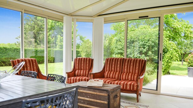 Et solarium med glasloft, to stribede sofaer, et træbord og et mønstret tæppe.