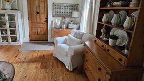 Een gezellige kamer met een houten vloer, een witte bank, een houten kastje met keramiek en een deur met raam.