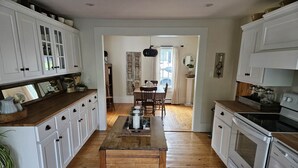 Een keuken met witte kastjes, houten aanrechtbladen, een centraal eiland en een eethoek met een tafel en stoelen.