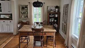 Een eetkamer met een houten tafel, stoelen, een hanglamp en uitzicht op het landschap door een raam.