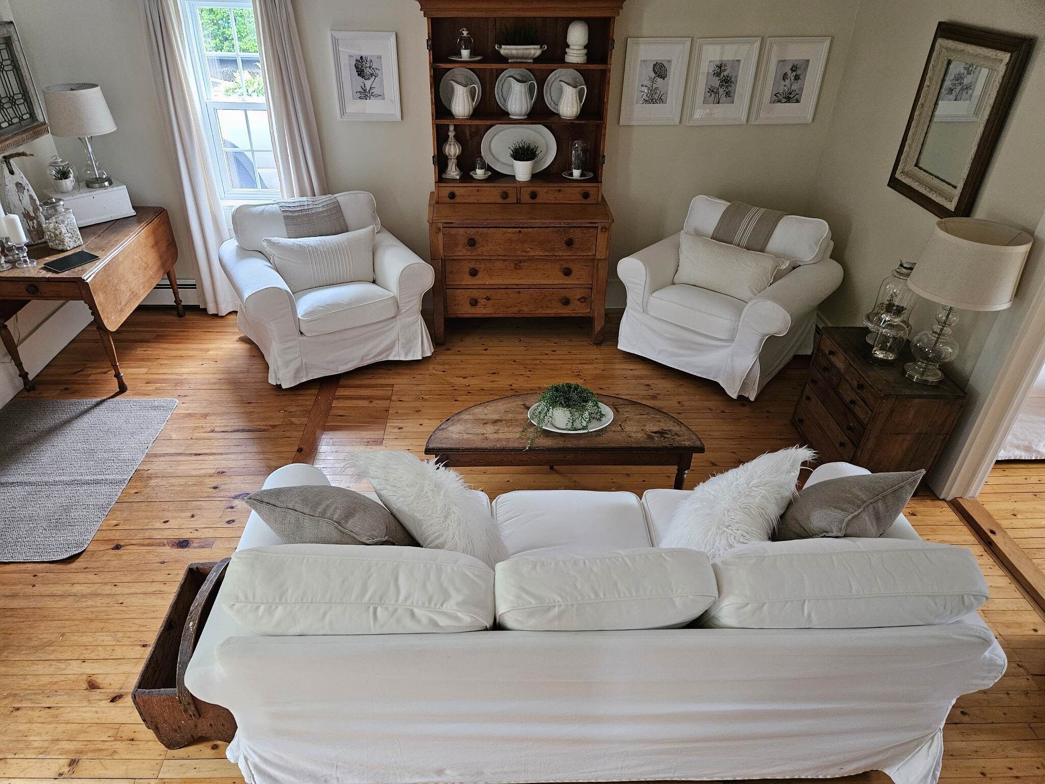 Un salon avec un canapé blanc, deux fauteuils blancs, une table basse en bois et un meuble en bois orné d’objets décoratifs.