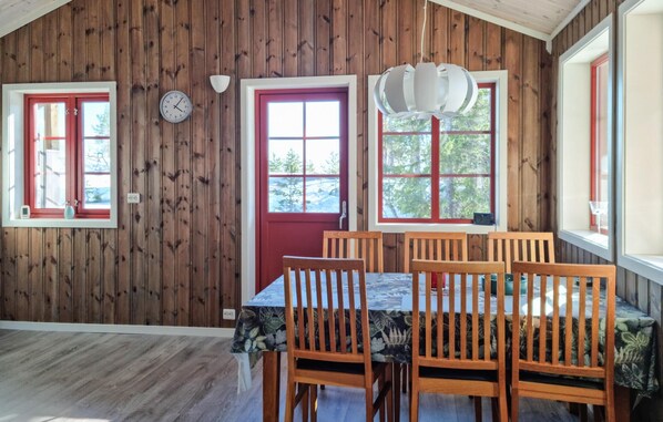 A dining area with wooden walls, a red door, and windows with red frames.