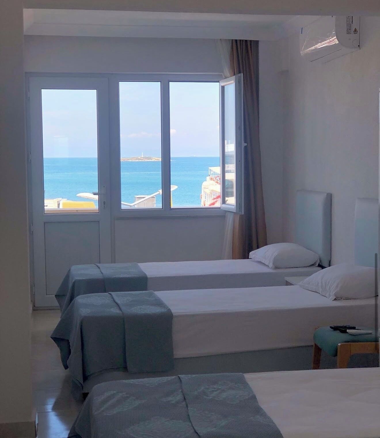 Habitación de hotel con dos camas, un ventanal grande con vistas al mar y un ventilador de techo.
