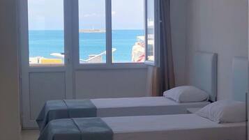 Habitación de hotel con dos camas, un ventanal grande con vistas al mar y un ventilador de techo.