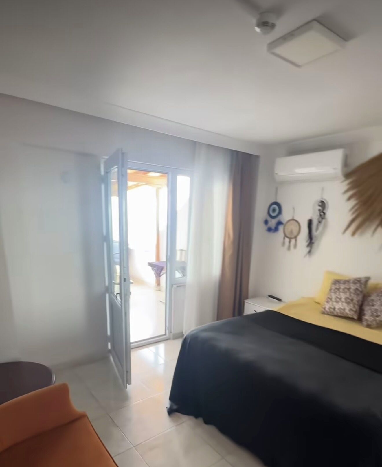 A bedroom with a bed, a chair, a door leading to a balcony, and a wall-mounted air conditioner.
