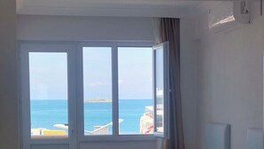 A room with two beds, a window with a view of the sea and a distant island, and an air conditioning unit on the wall. - Avşa apart otel (Marmara)