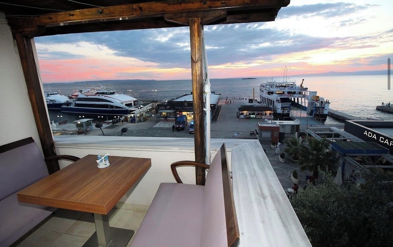A seaside restaurant with a view of the ocean and boats, featuring outdoor seating and a wooden table.