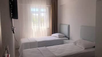 A hotel room with two beds, a TV, and a window with curtains.