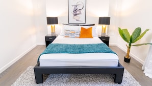 A modern bedroom with a bed, two bedside tables, a floor lamp, a framed artwork, and a potted plant. - Sovereign Cottage-Parking , Self Check-in  & Wifi (East Orange)