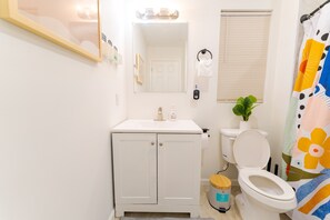 Un baño con lavamanos, inodoro y espejo blancos. Hay una cortina de ducha con diseño floral.