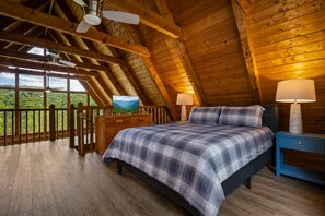 A bedroom with a bed, nightstands, a TV, and a view of the outdoors.