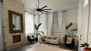 Un salon moderne avec un mur en briques blanches, un ventilateur de plafond, un canapé blanc et une table basse.