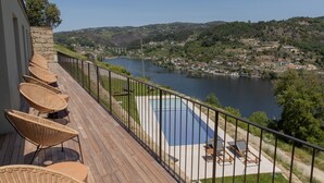 Terraza con sillas de mimbre y piscina con vista a un lago y una ciudad.