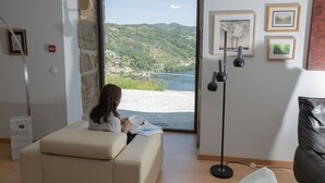 Una habitación con un amplio ventanal que da a un paisaje pintoresco, un sofá, una lámpara de pie y cuadros en la pared.