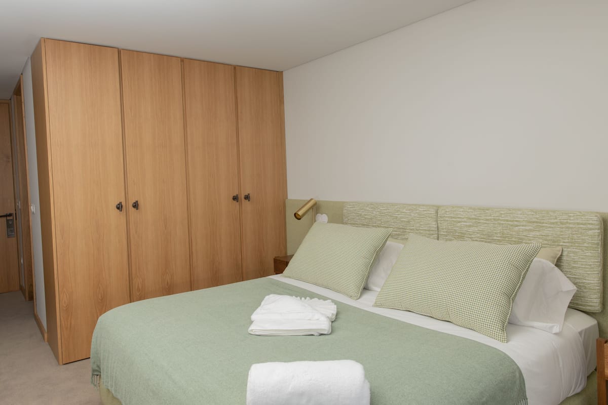 Un dormitorio con un amplio armario de madera, una cama con ropa de cama verde y una mesita de noche con una lámpara.