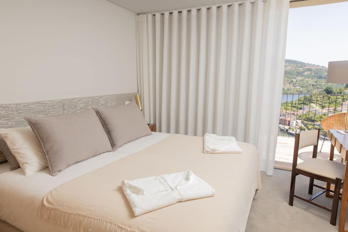 Habitación de hotel con una cama grande, vistas al paisaje y un balcón con una silla.