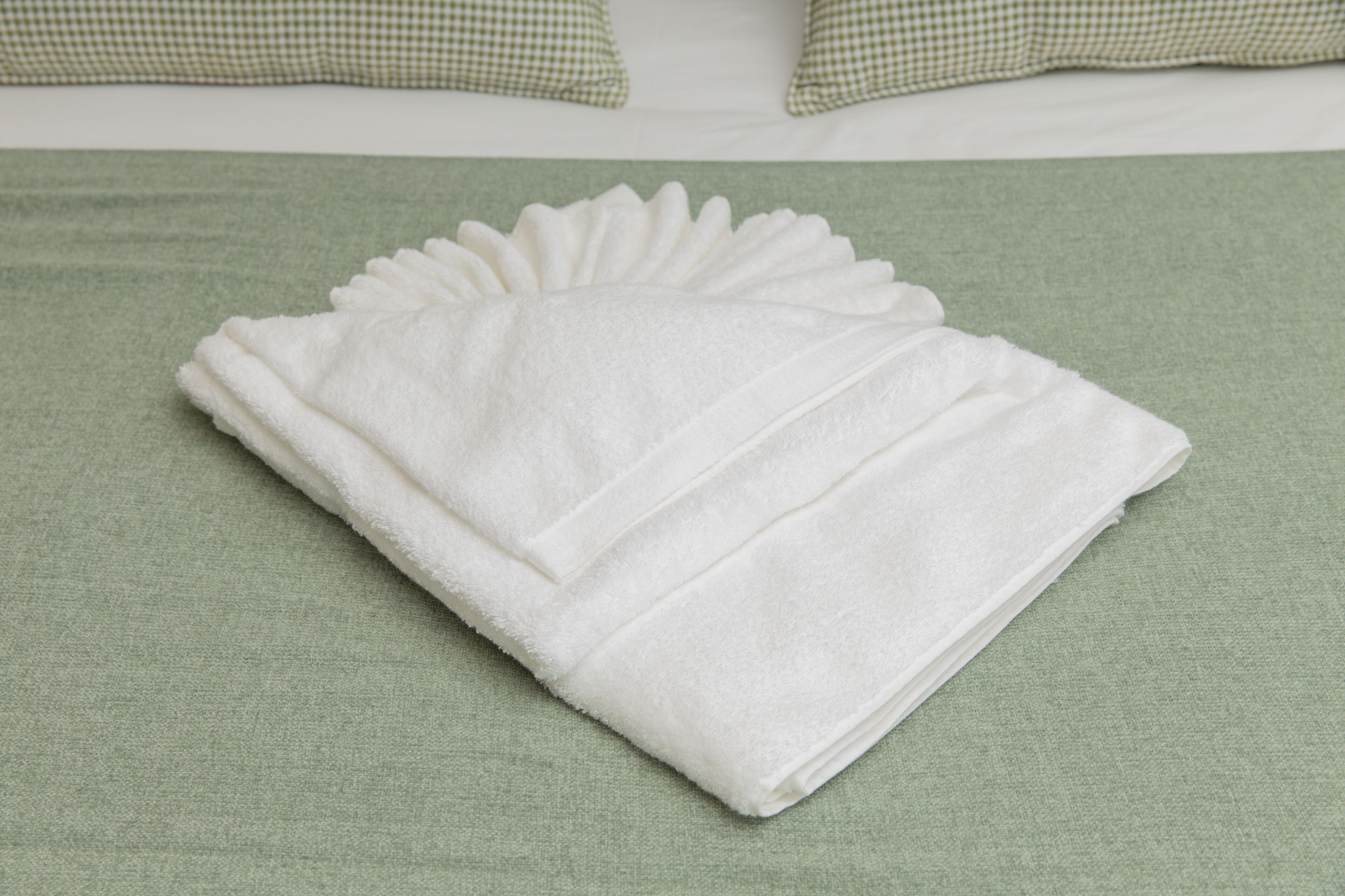 A neatly folded white towel on a green bedspread.