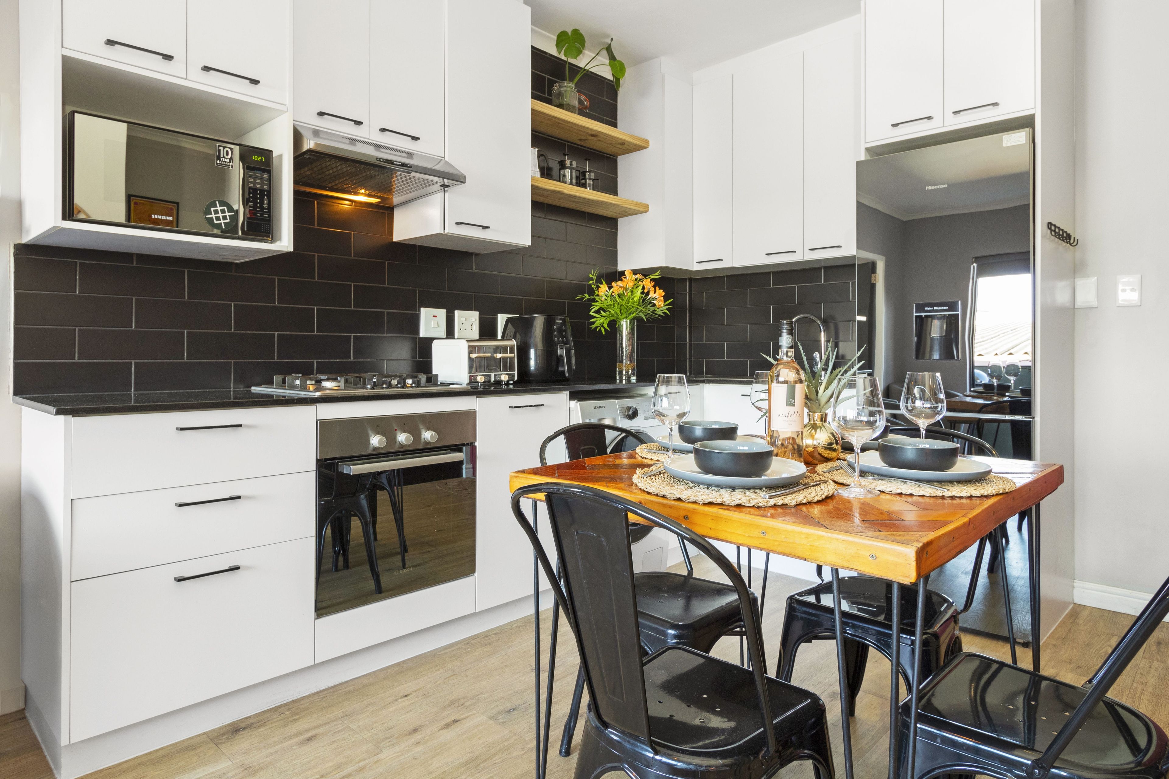 Una cocina moderna con armarios blancos, una mesa de comedor de madera y sillas negras.