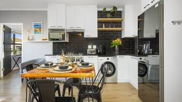 A modern kitchen with white cabinets, a wooden dining table, and a black tiled backsplash.
