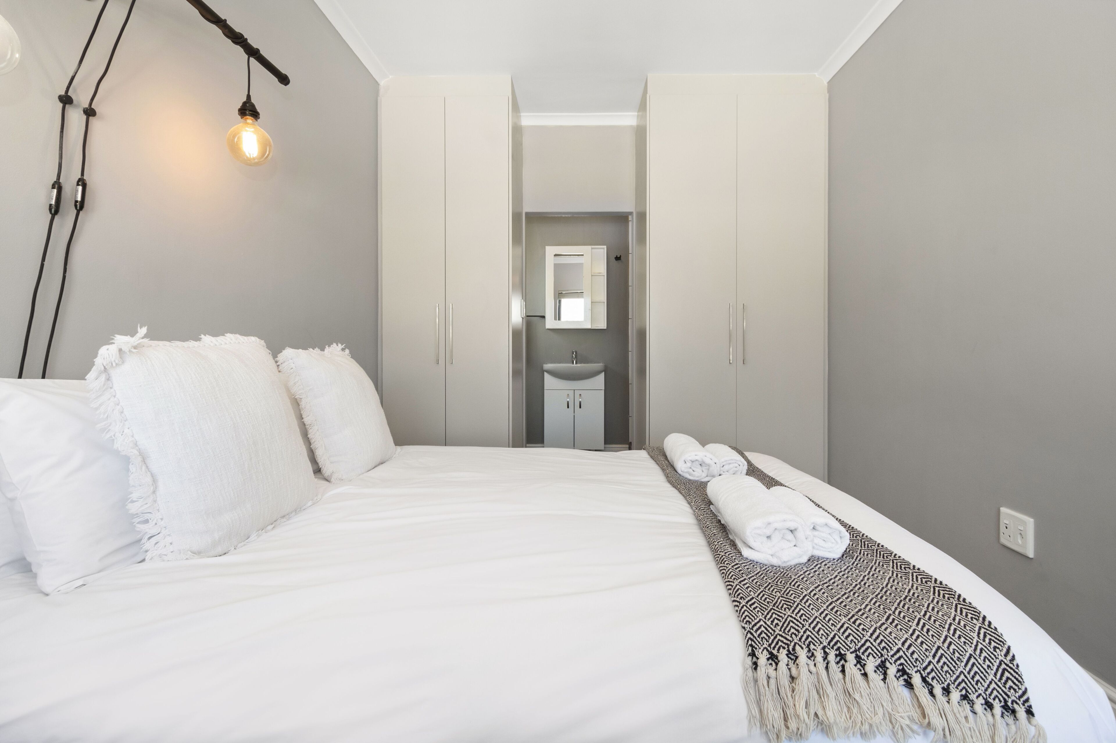 Et moderne hotelværelse med en stor seng, en senget lampe, et badeværelse med håndvask og spejl, samt et håndklædestativ.