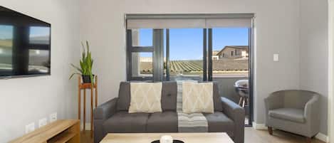 Una sala de estar moderna con un sofá, una mesa de centro, un televisor y vistas al exterior.