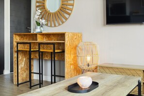 A modern room with a wooden dining table, a bar area with stools, a large mirror, and a wall-mounted TV. - Cape on Porterfield 5 (Cape Town)