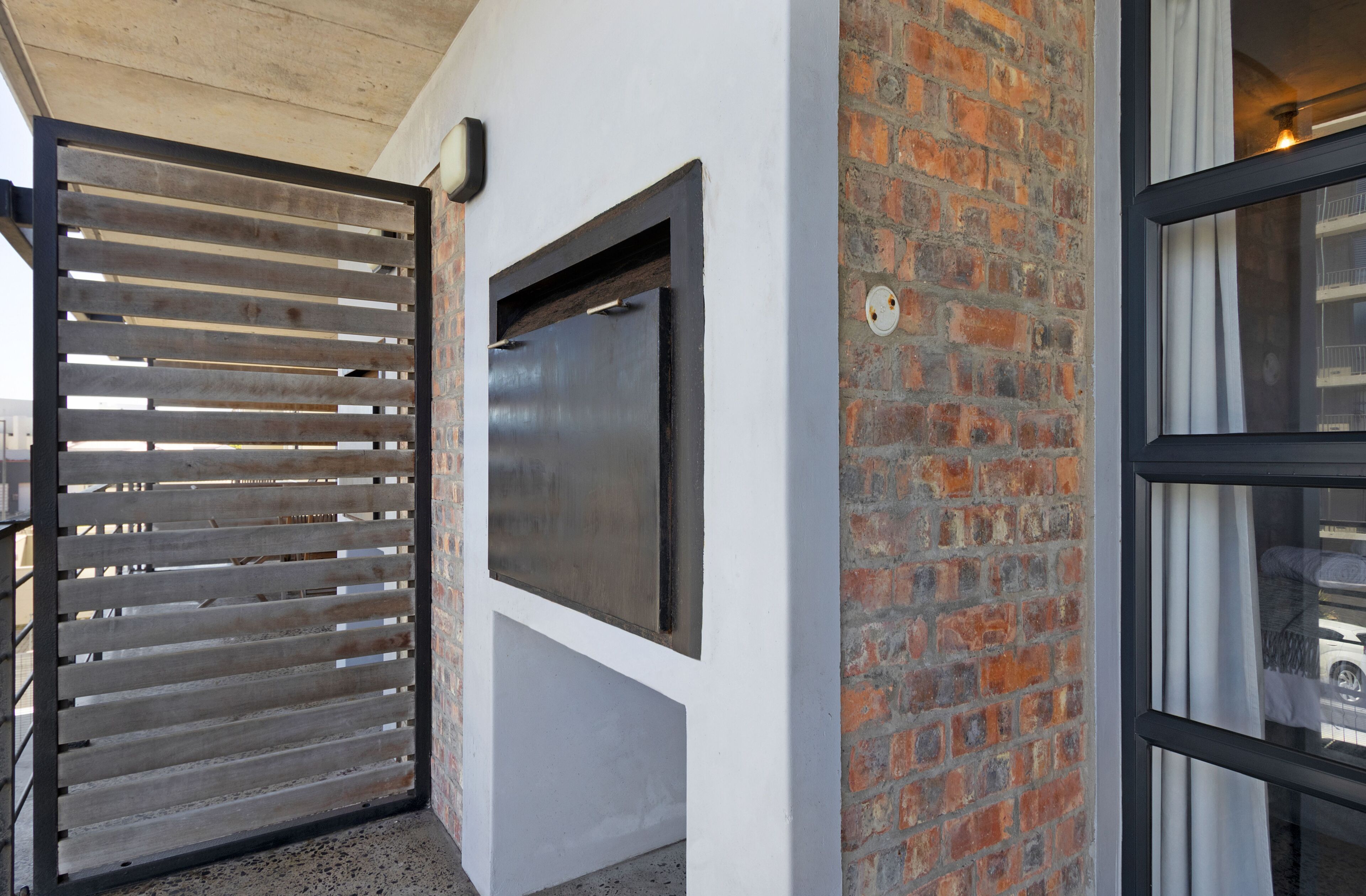 A modern building with a wooden slatted gate, a large metal-framed window, and a brick wall.