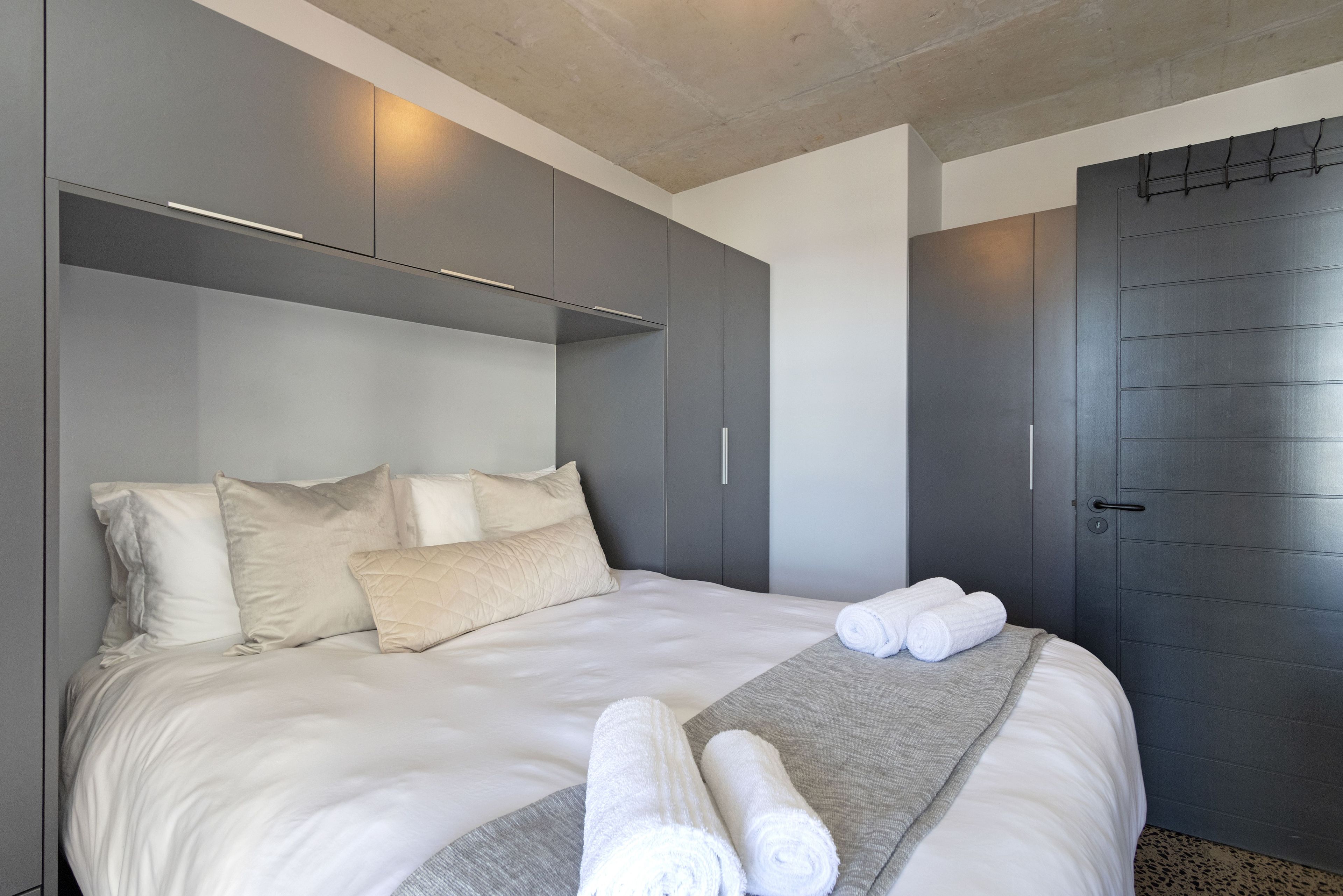 A modern hotel room with a large bed, grey wardrobe, and a door with a handle.