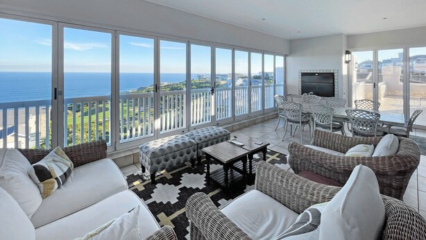 A spacious balcony with a sea view, furnished with wicker chairs and a sofa, and a flat-screen TV mounted on the wall. - Pinnacle Point Heritage Villa (Mossel Bay)