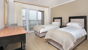 A hotel room with two beds, a wooden desk, and a balcony with curtains. - Pinnacle Point Heritage Villa (Mossel Bay)