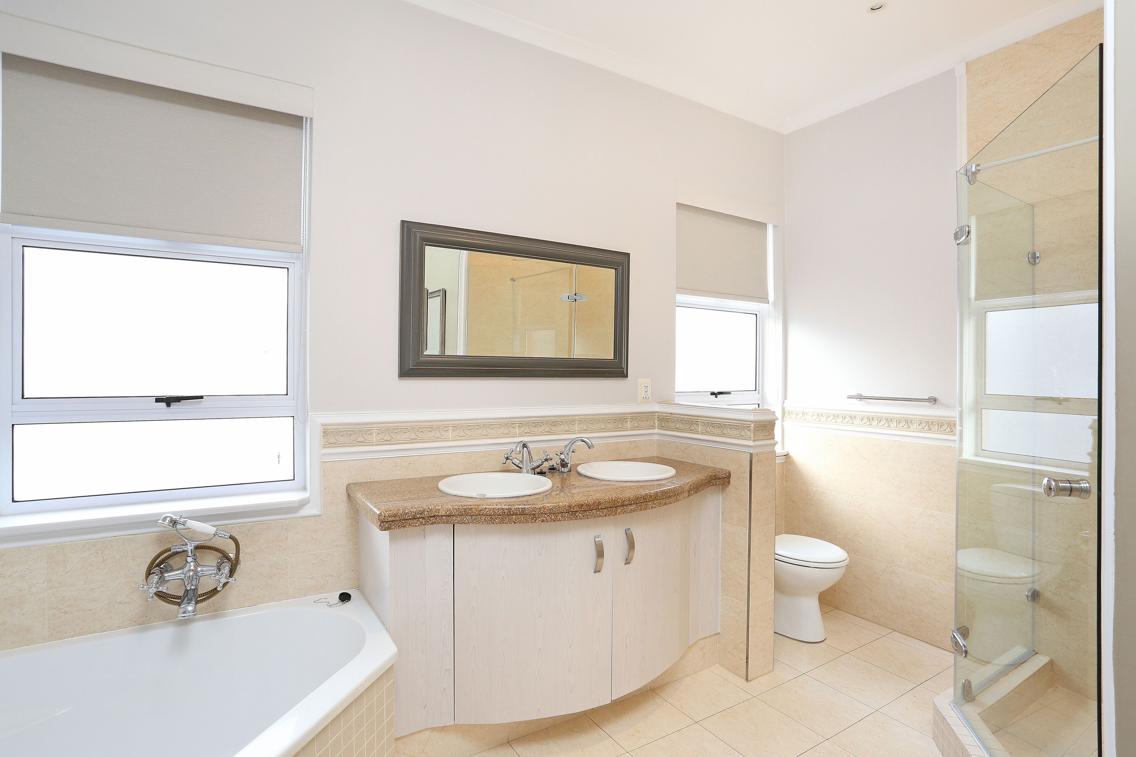 A bathroom with a bathtub, two sinks, a toilet, and a glass-enclosed shower.