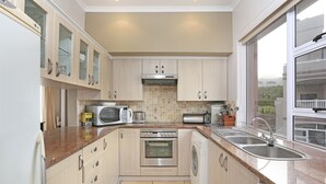 A modern kitchen with a built-in oven, microwave, and washing machine, featuring light wood cabinets and a large window. - Pinnacle Point Heritage Villa (Mossel Bay)