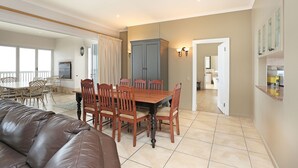 A dining area with a wooden table and chairs, a leather couch, and a kitchen in the background. - Pinnacle Point Heritage Villa (Mossel Bay)