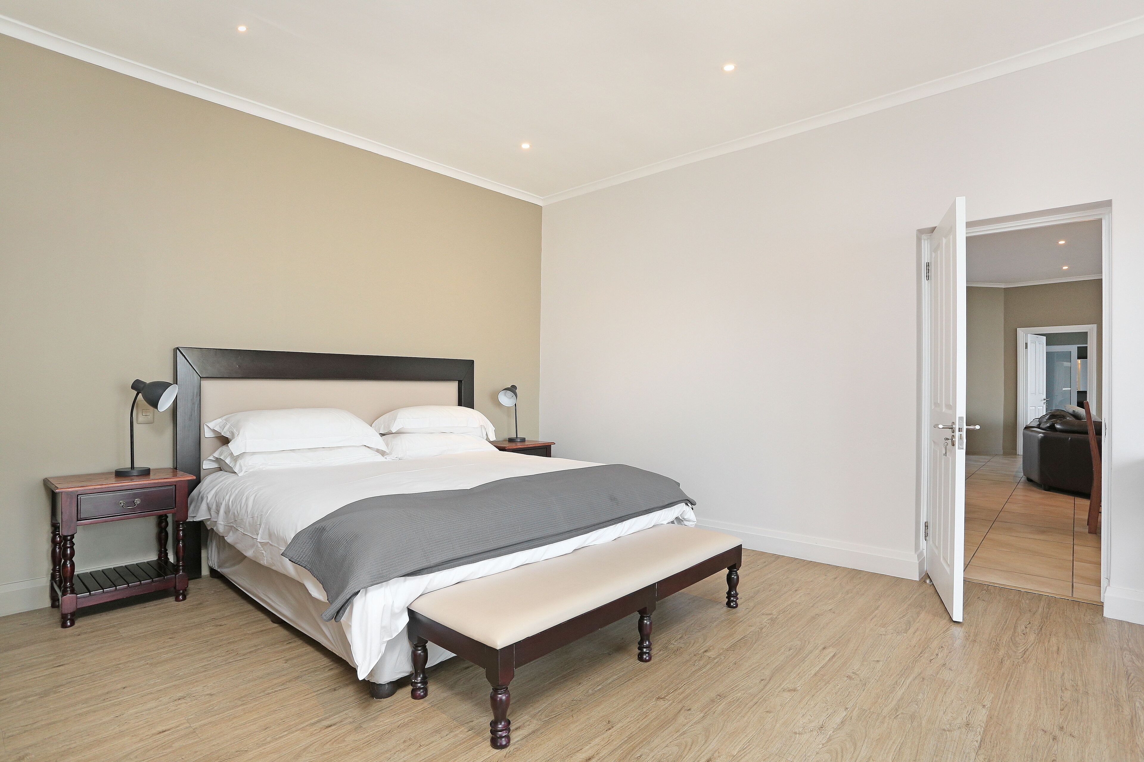 Une chambre à coucher comprenant un lit, des tables de chevet, un banc et une porte donnant sur une autre pièce.
