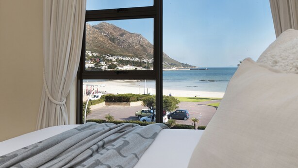 A hotel room with a large window offering a view of a beach, a parking area, and a mountain. - Summer Place 9 (Cape Town)