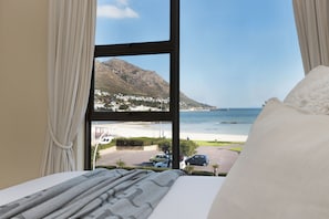 A hotel room with a large window offering a view of a beach, a parking area, and a mountain. - Summer Place 9 (Cape Town)