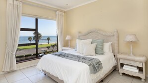 A bedroom with a large bed, two bedside tables with lamps, a view of the beach, and a balcony. - Summer Place 9 (Cape Town)
