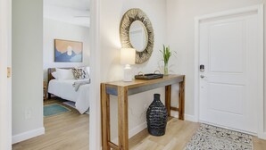 Hotellihuone, jossa on sänky, yöpöytä lampun kanssa, peili ja maljakko.