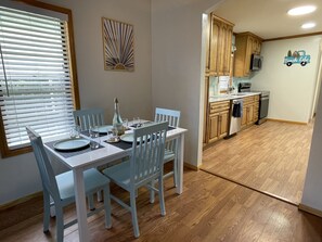 A dining area with a table set for four, a bottle of wine, and a decorative wall piece. - Gulfport Beach Getaway - Blocks to beach and casino, large yard & entertaintment (Gulfport)