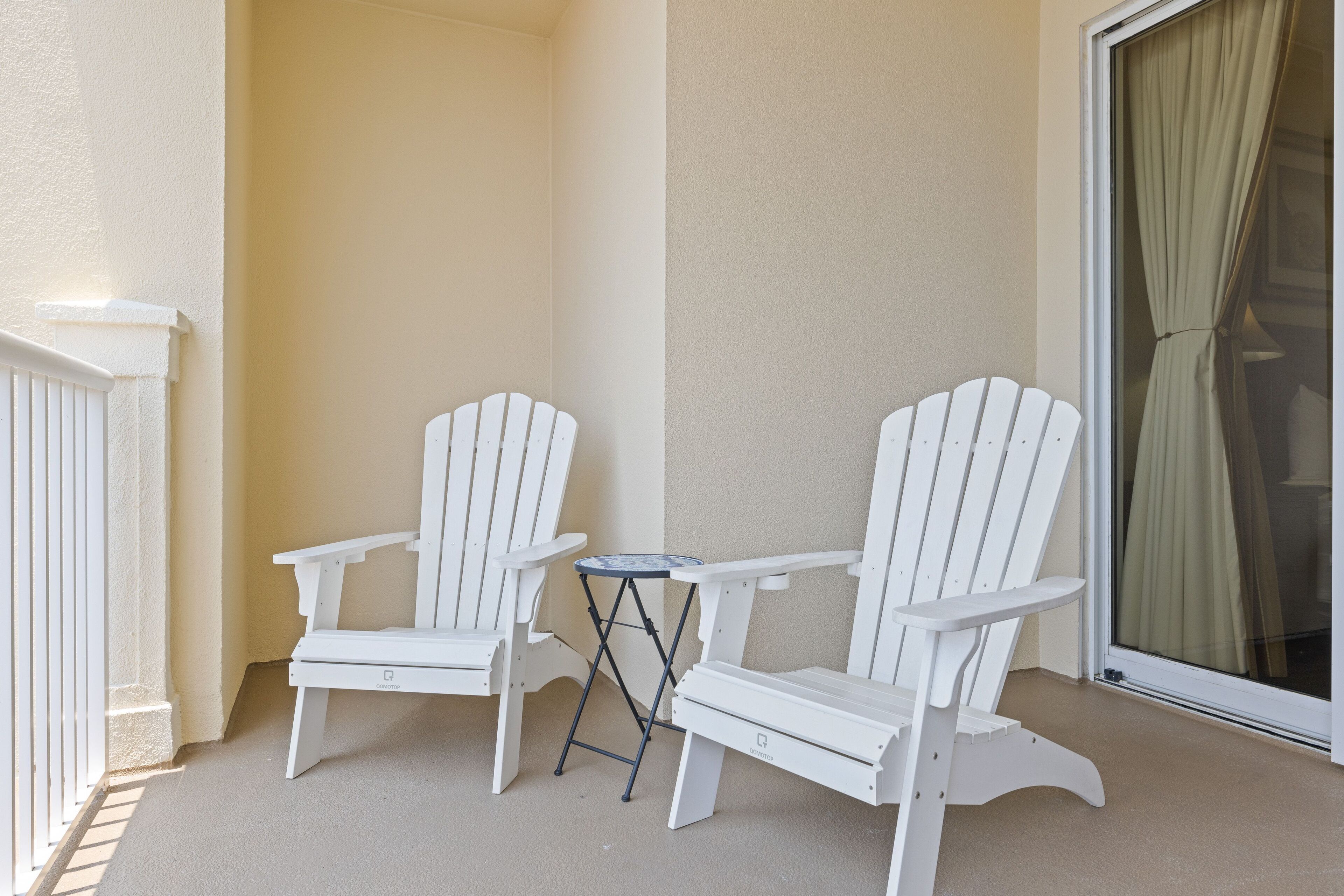 Un balcon avec deux fauteuils Adirondack blancs et une petite table ronde.
