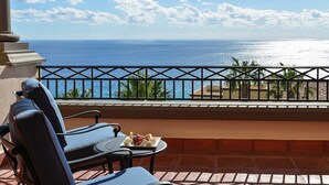 Un balcón con dos sillas, una mesa con un plato de comida y vista al océano.