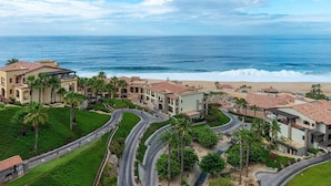 Un resort costero con varias edificaciones, palmeras y un camino curvo que lleva a la playa.