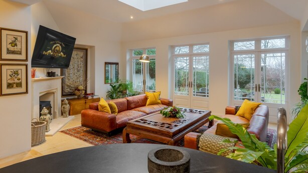 Amplia sala de estar con techo alto, ventanas grandes, chimenea y diversas opciones de asientos.