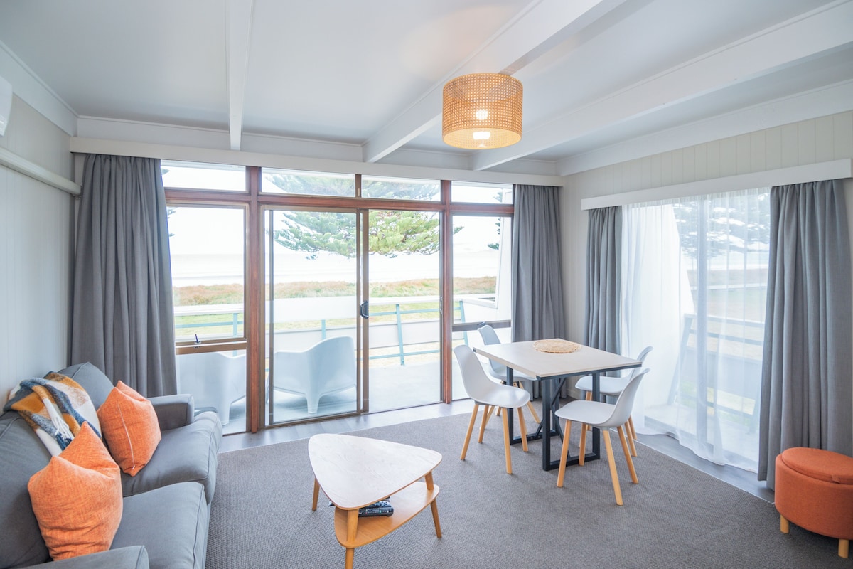 Ein modernes Hotelzimmer mit einer Couch, einem Esstisch, Stühlen und Blick durch große Fenster.